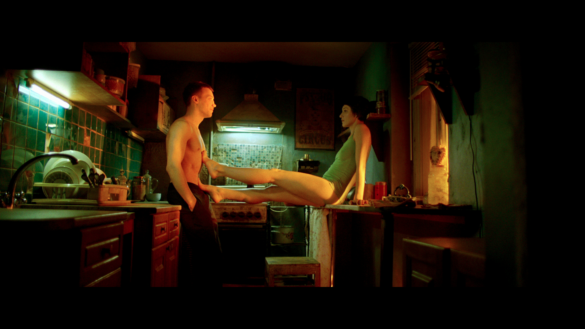 Guy stands opposite woman who sits on the kitchen counter with her legs stretched out.